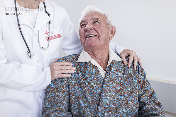 Arzt und lächelnder älterer Patient im Rollstuhl
