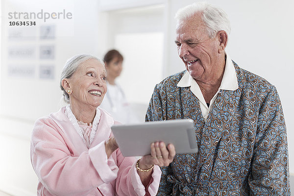 Arzt und lächelnder älterer Patient im Rollstuhl mit digitalem Tablett