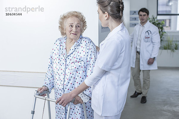 Krankenschwester leitende ältere Patientin mit Gehhilfe auf dem Krankenhausboden