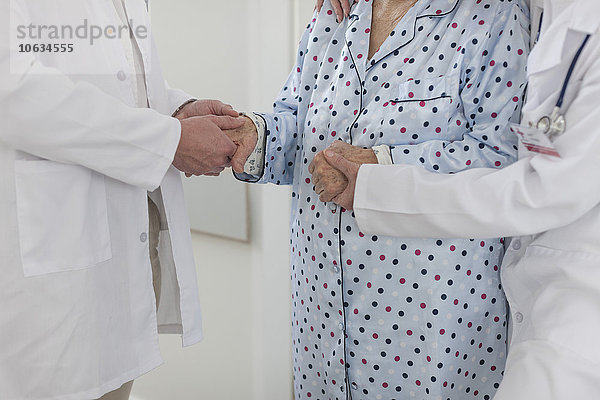 Zwei Ärzte  die Hände eines älteren Patienten halten