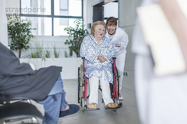Arzt mit älterer Patientin im Rollstuhl auf dem Krankenhausboden