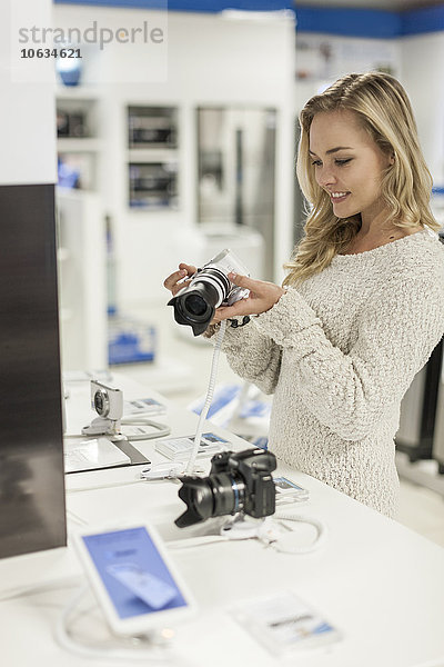 Junge Frau beim Betrachten einer Kamera in einem Geschäft