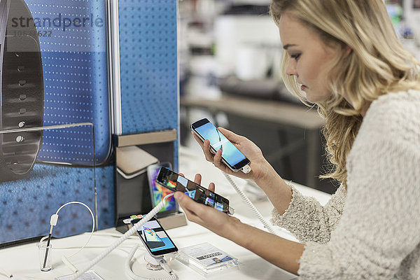 Junge Frau vergleicht zwei Smartphones in einem Geschäft