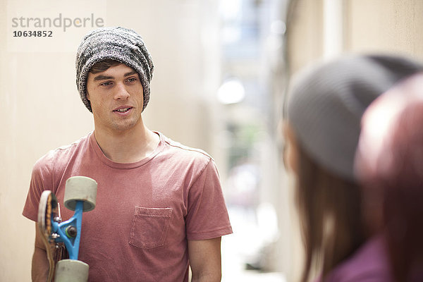 Junger Mann mit Skateboard in einem Gang im Gespräch mit Freunden