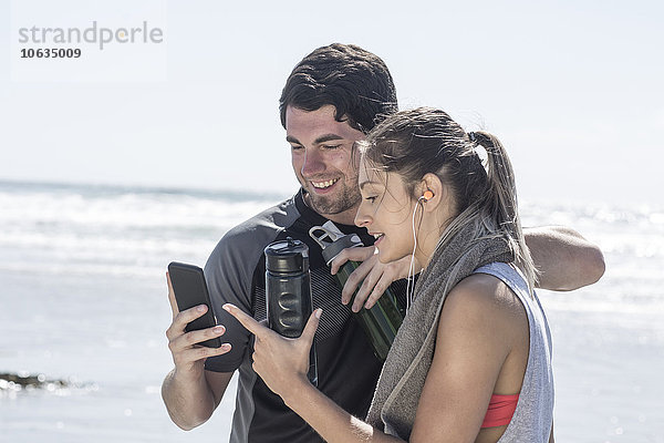 Sportlicher Mann und Frau am Strand mit Blick auf das Handy