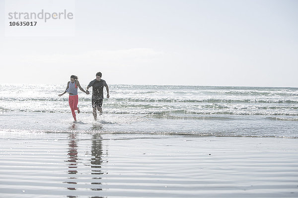 Junger Mann und Frau laufen Hand in Hand im Ozean