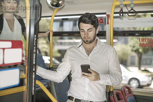 Junger Mann im Stadtbus hört Musik vom Smartphone