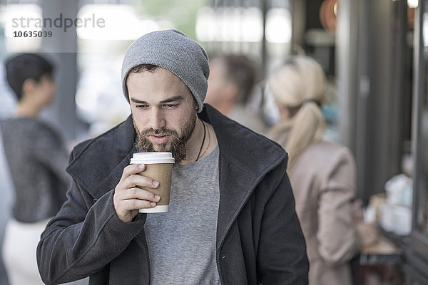 Junger Mann trinkt Kaffee zum Mitnehmen in der Stadt