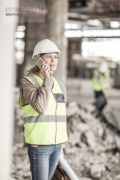 Frau in Arbeitsschutzbekleidung am Handy auf der Baustelle