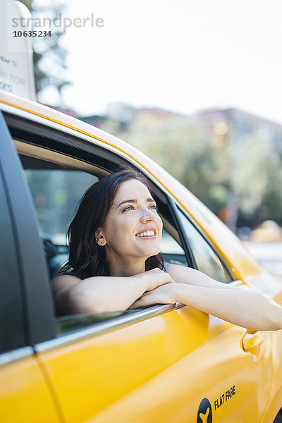 USA  New York City  Porträt einer lächelnden jungen Frau  die durch das Fenster eines gelben Taxis schaut.