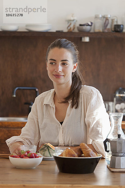Junge Frau am Esstisch sitzend mit Frühstück  lächelnd