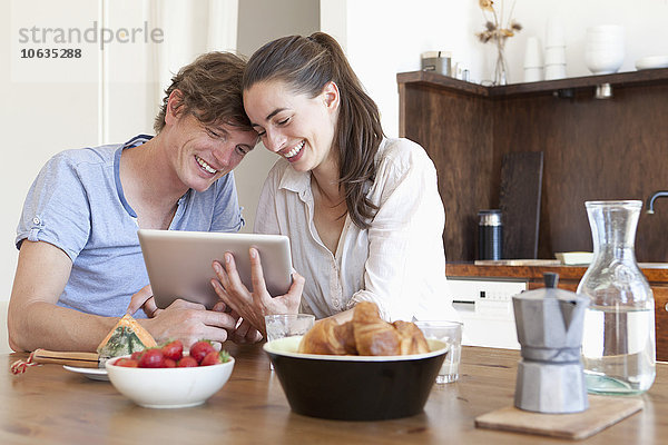 Junges Paar am Esstisch sitzend  mit digitalem Tablett