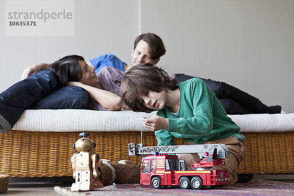 Junge spielt mit Spielzeug  Mutter und Vater liegen auf dem Sofa im Hintergrund