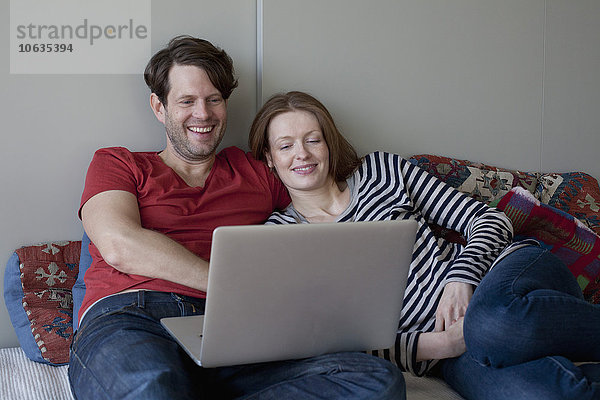 Paar mit Laptop auf dem Sofa liegend