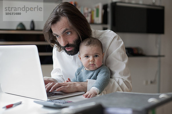 Mann arbeitet am Laptop  während er mit einem kleinen Mädchen zu Hause sitzt.