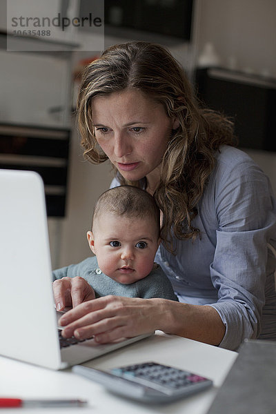 Frau arbeitet am Laptop  während sie mit dem kleinen Mädchen zu Hause sitzt.