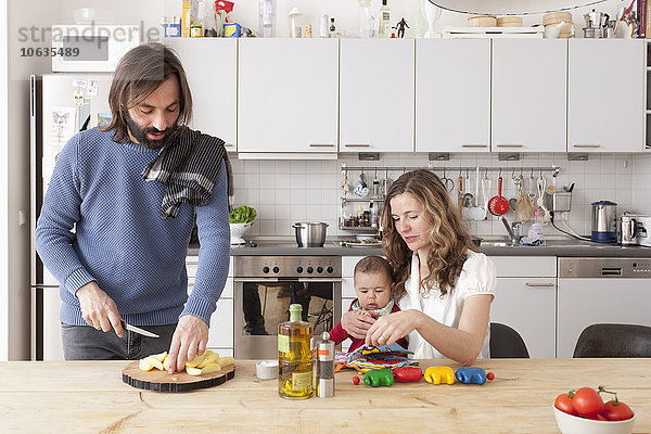 Vater beim Gemüsehacken mit Mutter und Baby in der Küche