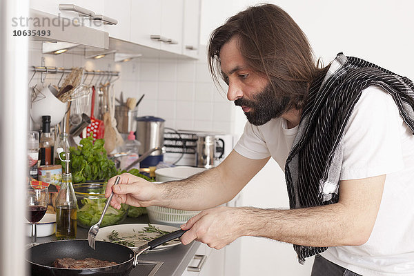 Mittlerer erwachsener Mann bei der Zubereitung von Fleisch in der heimischen Küche