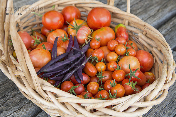 Hochwinkelansicht von frischen Tomaten und violetten Bohnen im Weidenkorb