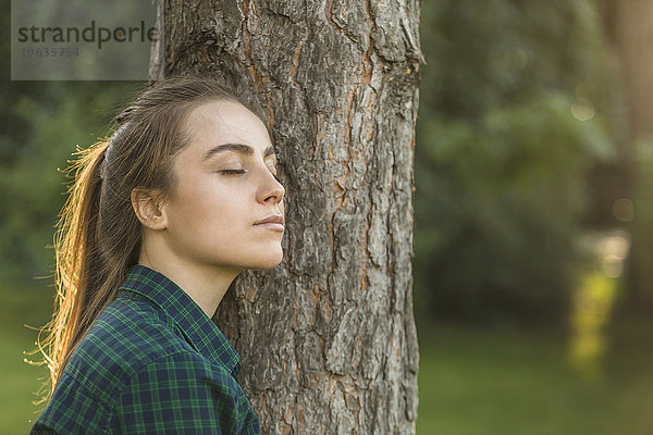 Schöne Frau mit geschlossenen Augen  die sich am Baumstamm des Parks lehnt