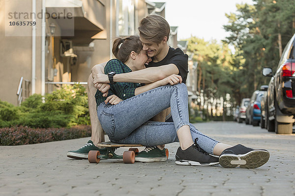 Glückliches junges Paar  das sich auf dem Skateboard im Freien umarmt.