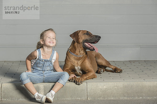 Glückliches Mädchen sitzend mit Hund auf dem Bürgersteig im Freien