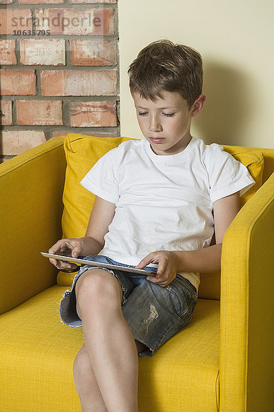 Junge mit digitalem Tablett im Sessel zu Hause