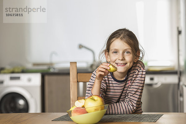 Porträt eines glücklichen Mädchens beim Apfelessen am Tisch