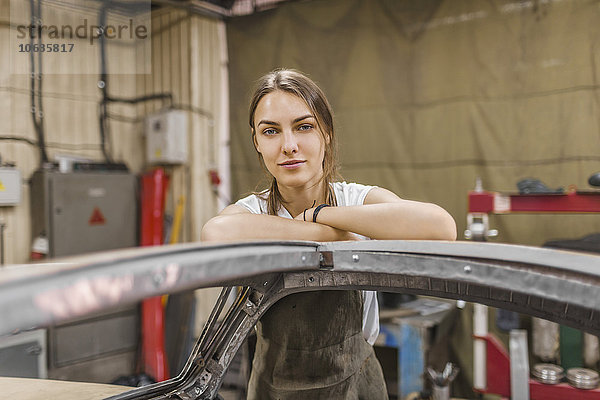 Porträt einer selbstbewussten Mechanikerin  die sich auf das Auto in der Garage stützt.