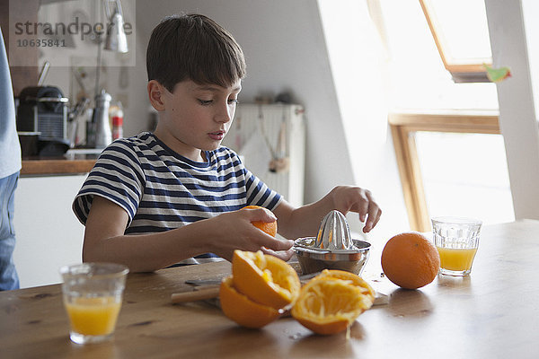 Junge macht Orangensaft am Tisch im Haus