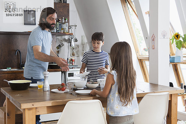 Vater und Kinder decken den Tisch für das Mittagessen in der Küche.