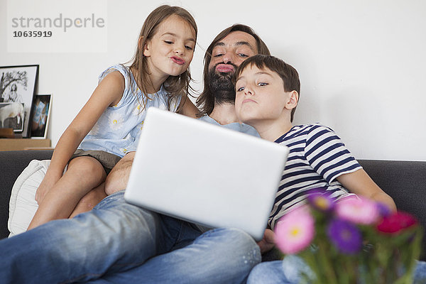 Vater mit Kindern  die auf dem Sofa vor dem Laptop kräuseln