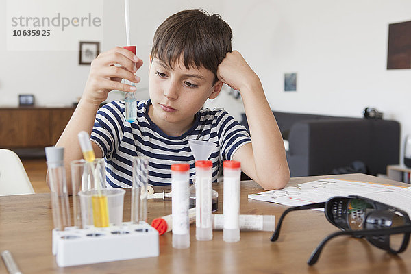 Junge schaut auf das Reagenzglas  während er zu Hause ein wissenschaftliches Experiment durchführt.