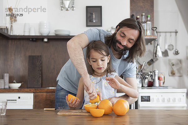 Vater hilft Tochter beim Auspressen von Orangen in der Küche