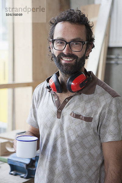 Porträt eines glücklichen mittelgroßen Schreiners beim Kaffee in der Werkstatt