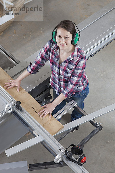 Hochwinkelporträt einer glücklichen Schreinerin mit einer Formatkreissäge in der Werkstatt