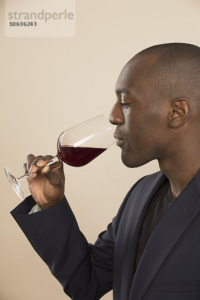 Gut gekleideter Mann bei der Verkostung von Rotwein vor farbigem Hintergrund