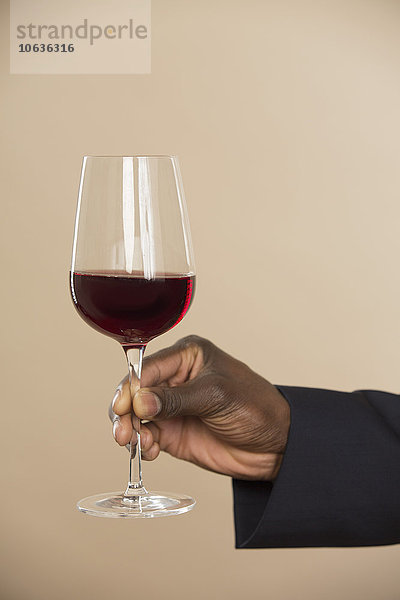 Abgeschnittene Hand mit rotem Weinglas vor farbigem Hintergrund