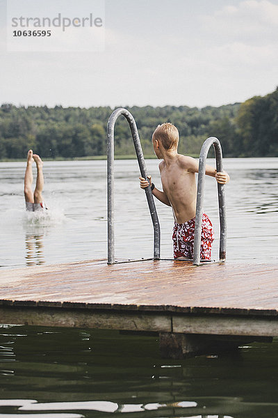 Junge  der einen Freund ansieht  der Beine aus dem See ragt.