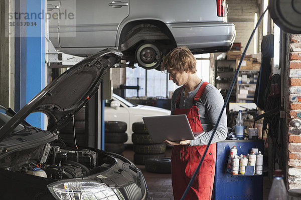 Mechaniker mit Laptop bei der Untersuchung des Fahrzeugmotors in der Werkstatt