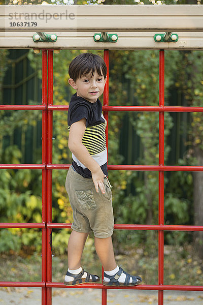 Porträt eines Jungen  der auf einer Kletterwand im Park steht