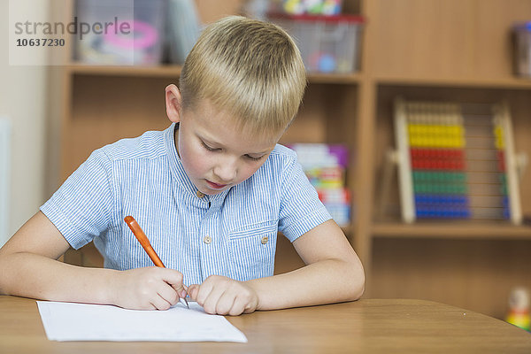 Konzentrierter Junge beim Schreiben auf Papier am Tisch