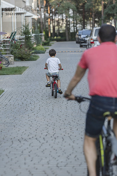 Rückansicht von Vater und Sohn beim Fahrradfahren auf der Straße