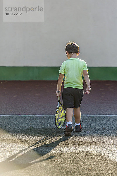 Rückansicht des Jungen mit Tennisschläger und Spaziergang auf dem Platz