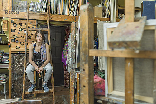 Künstlerin sitzend auf Leiter im Atelier