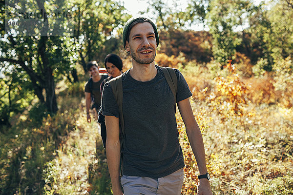 Lächelnder junger Mann beim Wandern mit Freunden im Wald