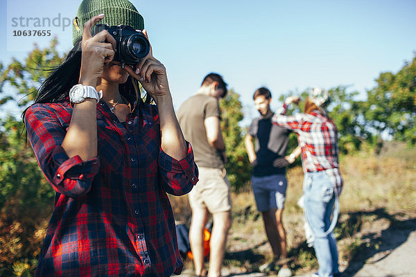 Junge Frau beim Fotografieren  während Freunde im Hintergrund stehen