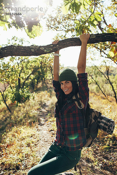 Porträt einer lächelnden Frau  die vom Ast im Wald schwingt.