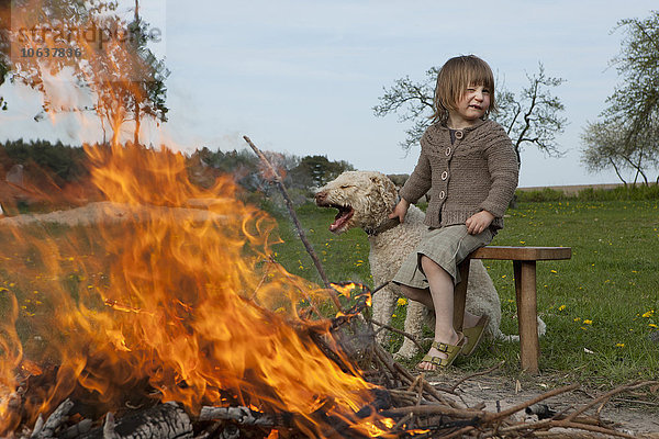 Mädchen und Hund sitzend am Lagerfeuer auf dem Feld