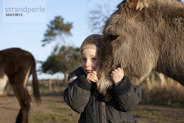 Süßes Mädchen umarmt Esel auf dem Feld